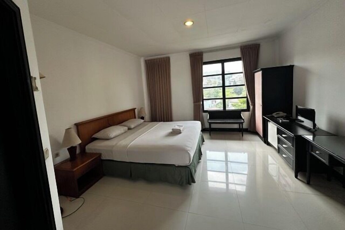 A hotel room with a bed, a desk, a television, and a window with curtains.