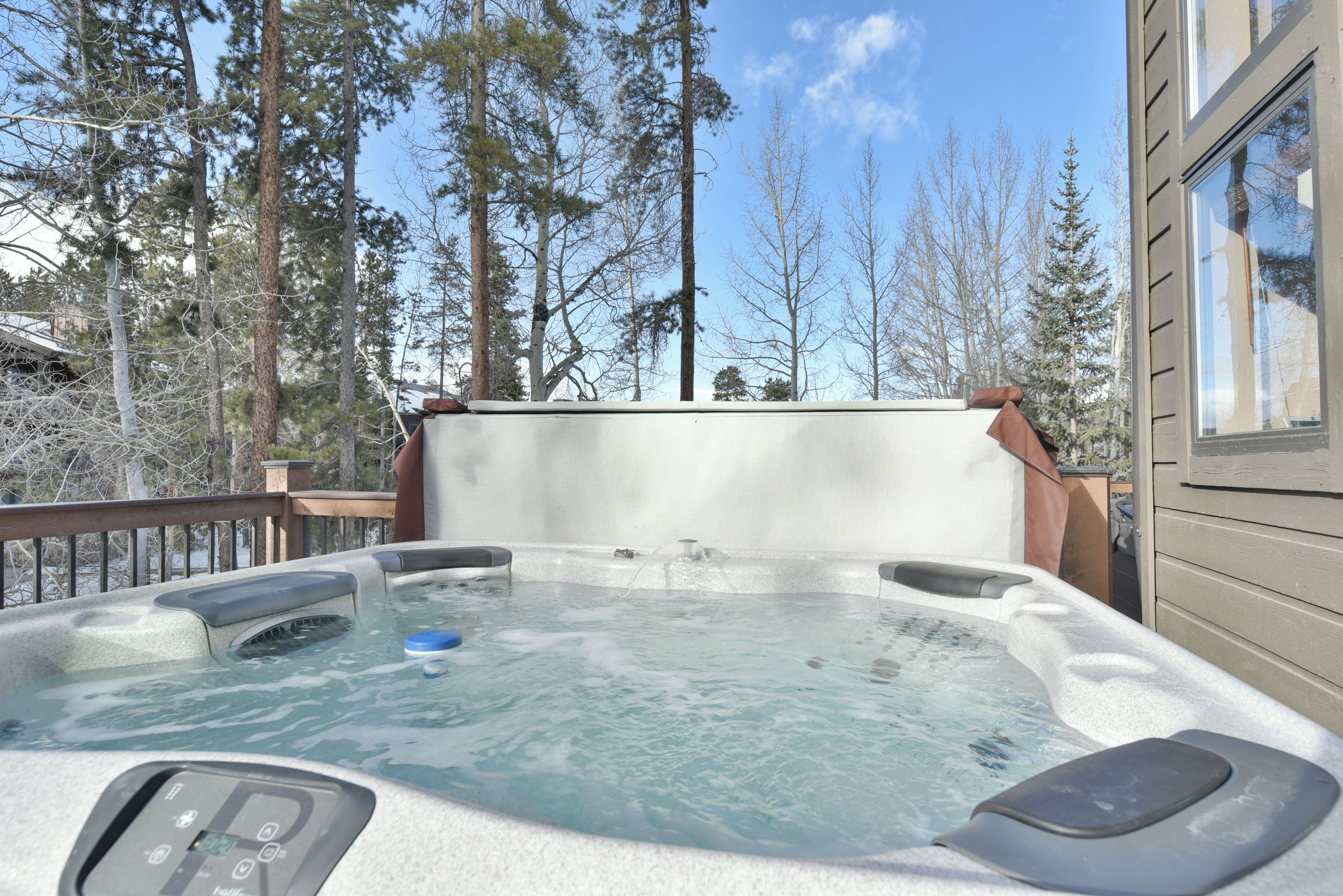 A hot tub on a deck with a view of tall trees and a building in the background.