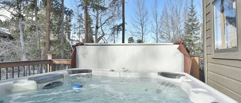 Un jacuzzi en una terraza con vistas a altos árboles y un edificio al fondo.