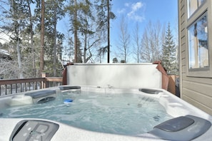 A hot tub on a deck with a view of tall trees and a building in the background.