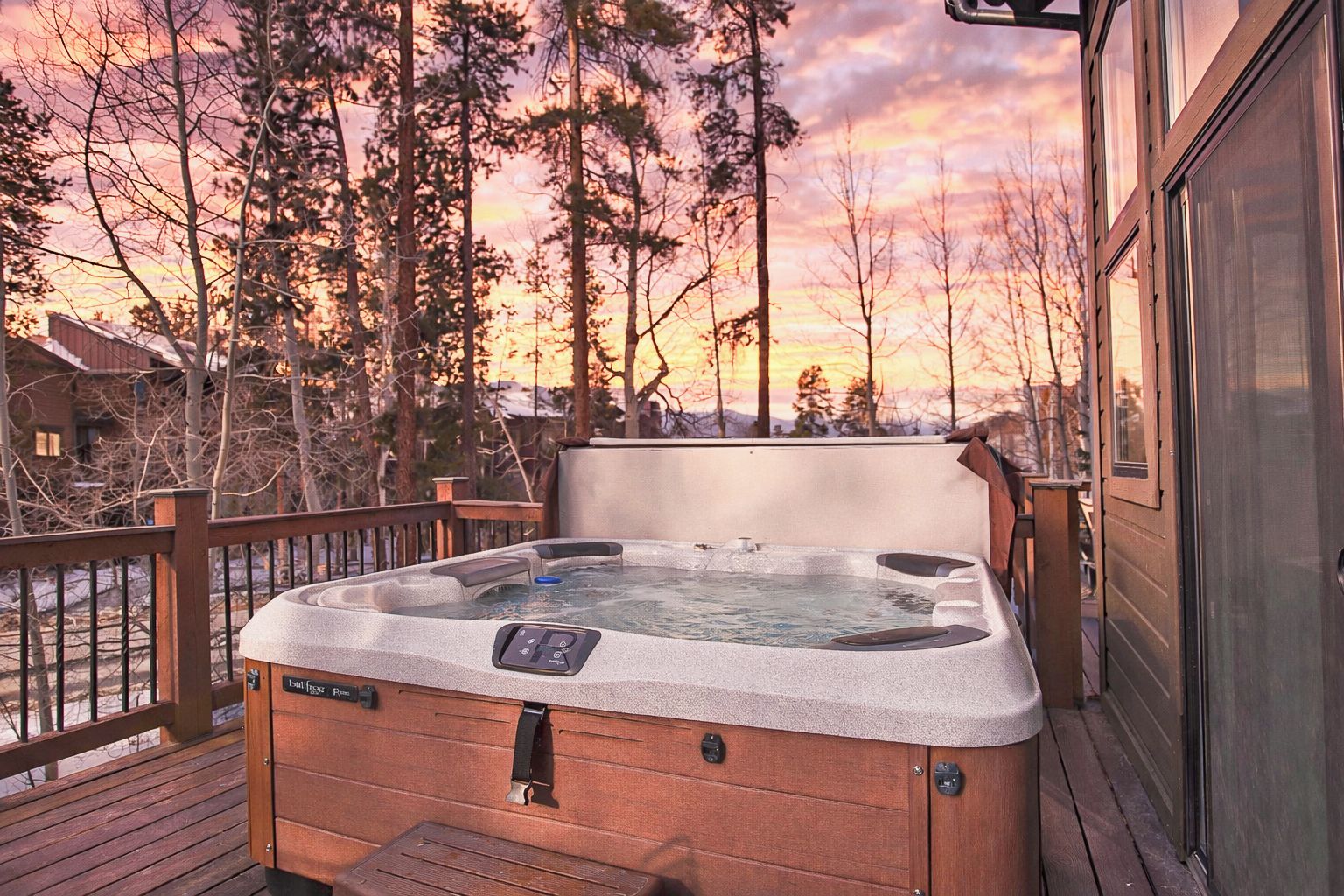 A hot tub on a wooden deck with a view of trees and a sunset.