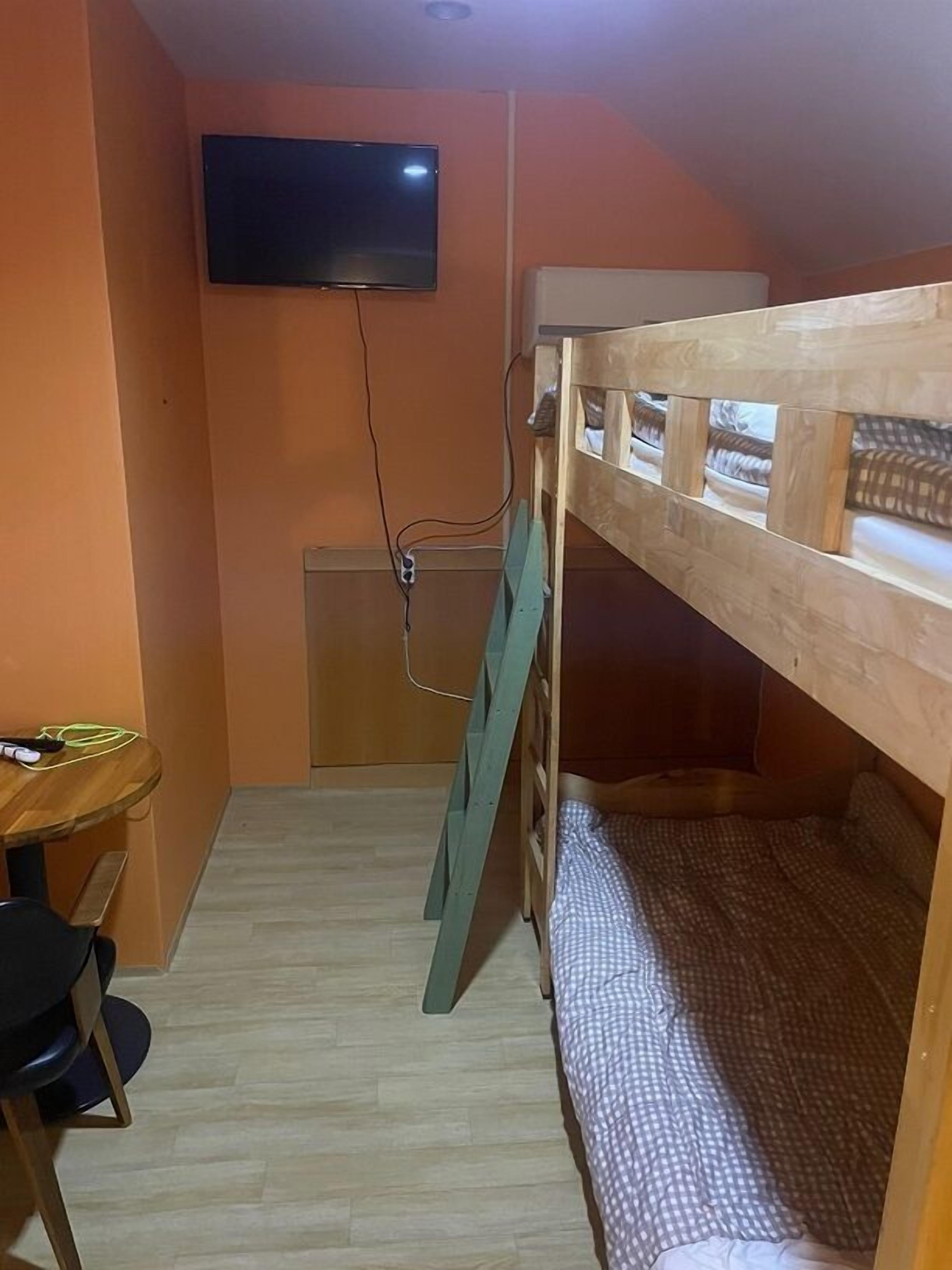 A room with a bunk bed, a desk, and a television mounted on the wall.