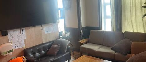 A living room with two couches, a wooden coffee table, a flat-screen TV mounted on the wall, and a window with curtains.