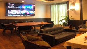Hotellihuoneessa on puinen ruokapöytä, nahkasohva ja seinälle asennettu televisio, josta näkyy useita kanavia.