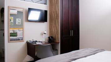 A hotel room with a bed, a desk with a chair, a television, a mirror, and a wardrobe.
