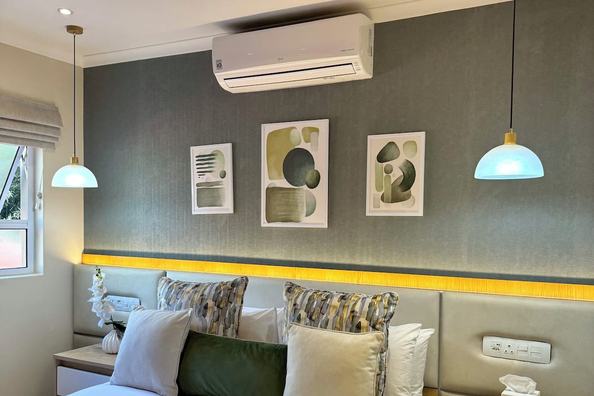 Une chambre d’hôtel moderne dotée d’un grand lit, de tables de chevet, d’un climatiseur mural et de trois œuvres d’art abstraites encadrées.
