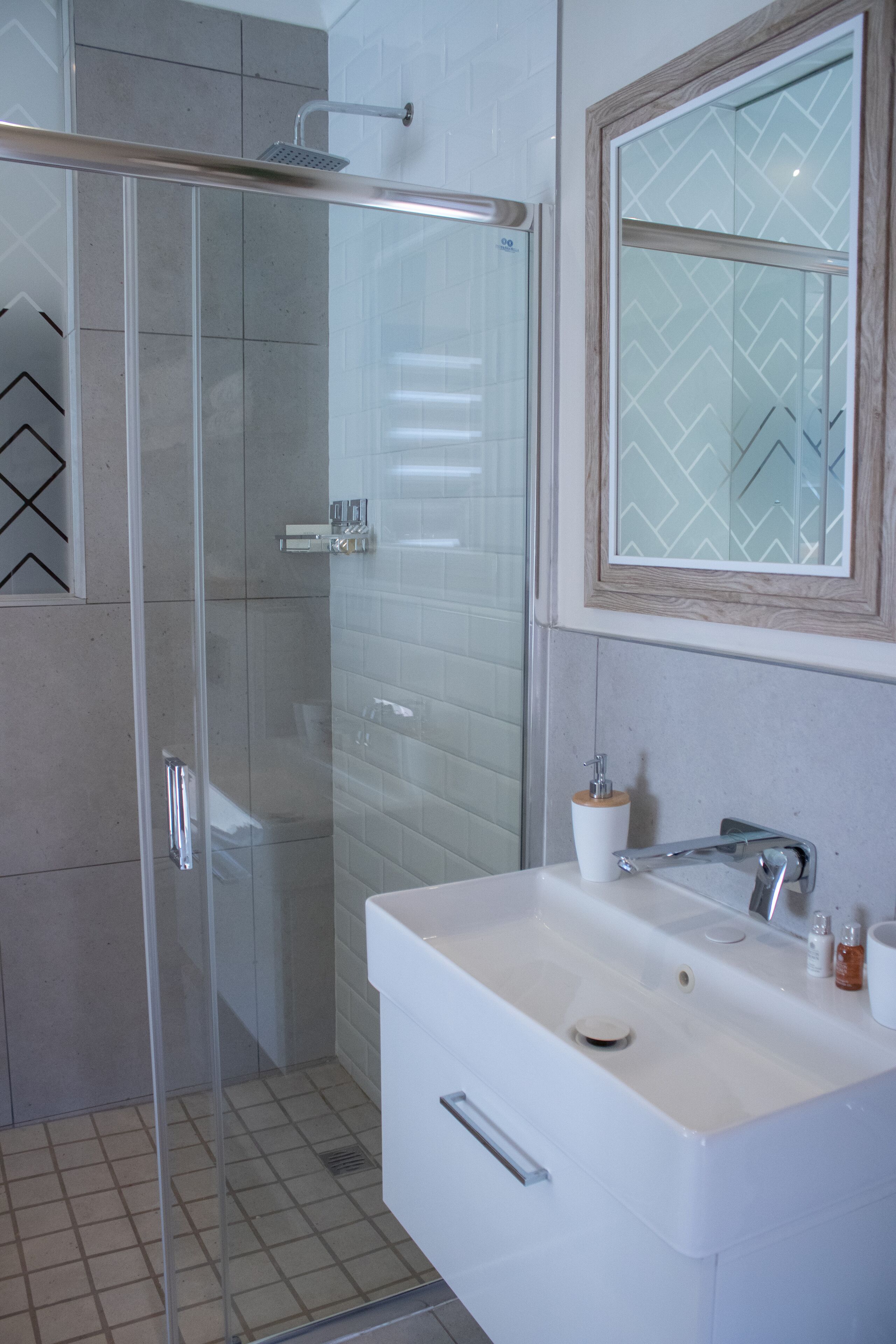 A modern bathroom with a glass shower enclosure, a white sink with a mirror, and a tiled floor.
