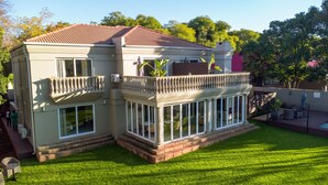 A two-story house with a balcony, large windows, and a well-maintained lawn. - 1945 On Kloof Guesthouse (Johannesburg)
