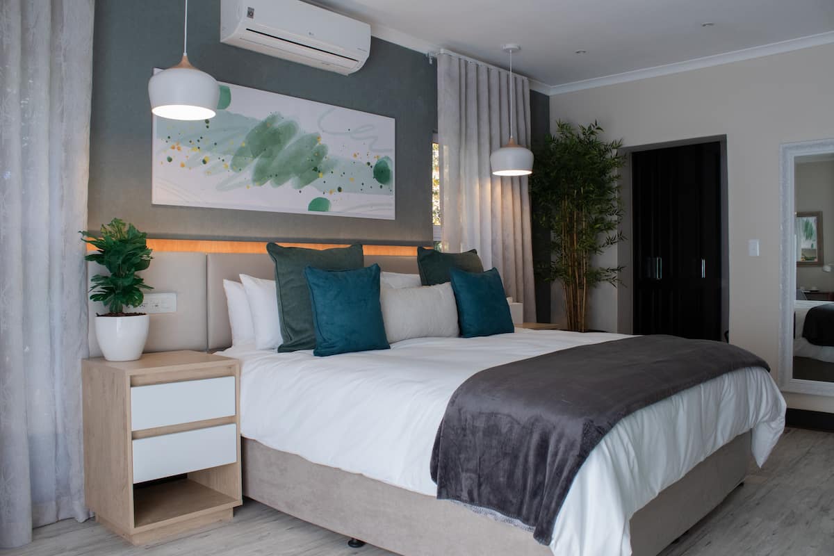 Une chambre moderne avec un grand lit, des tables de chevet, une plante en pot et un climatiseur fixé au mur.
