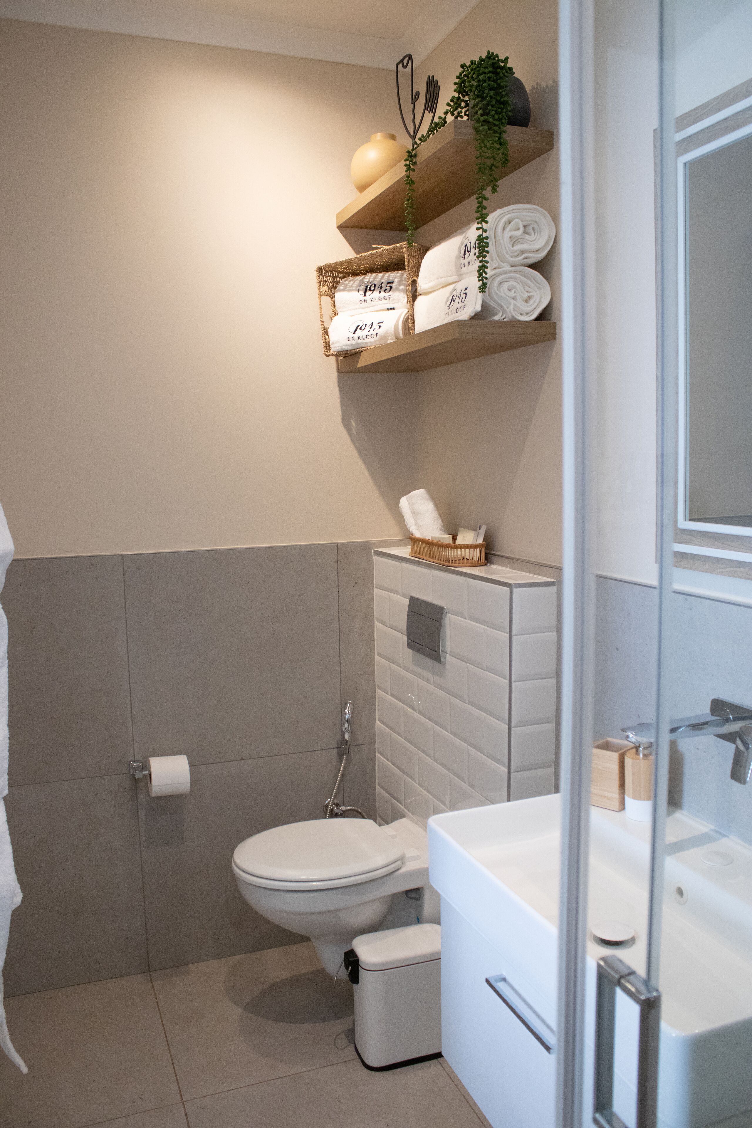 Un baño con inodoro, lavabo y bañera. Hay toallas y una planta en los estantes.