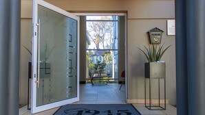 A hotel entrance with a glass door, a welcome mat, a bench, and a potted plant. - 1945 On Kloof Guesthouse (Johannesburg)