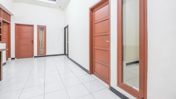 A hallway with white tiled flooring, wooden doors, and a skylight. - Hotel O Transit 1 (Makassar)