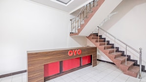 A reception desk with a wooden finish and a red accent panel, a staircase with a metal railing, and a tiled floor. - Hotel O Transit 1 (Makassar)