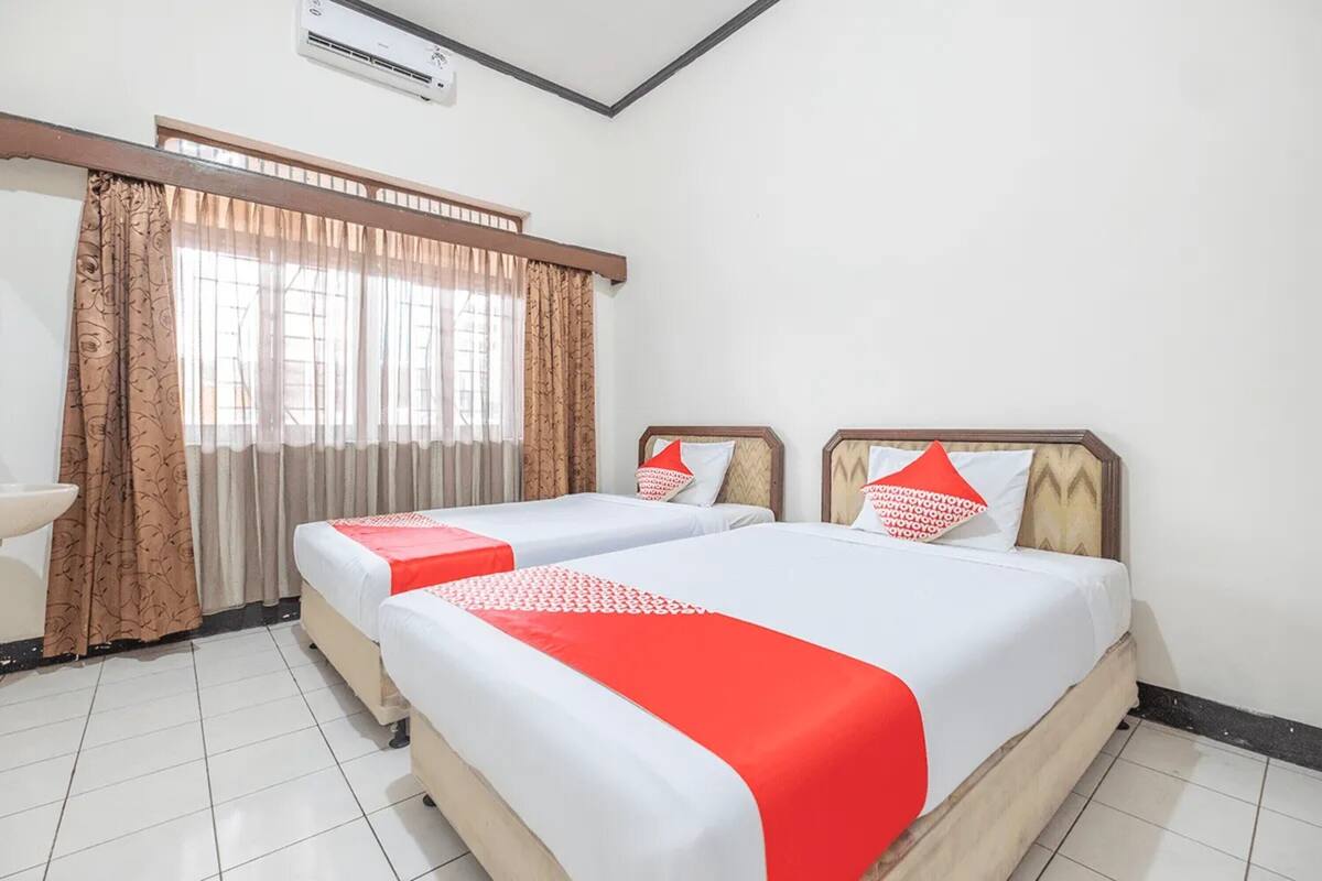A hotel room with two beds, a window with curtains, a sink, and an air conditioning unit.