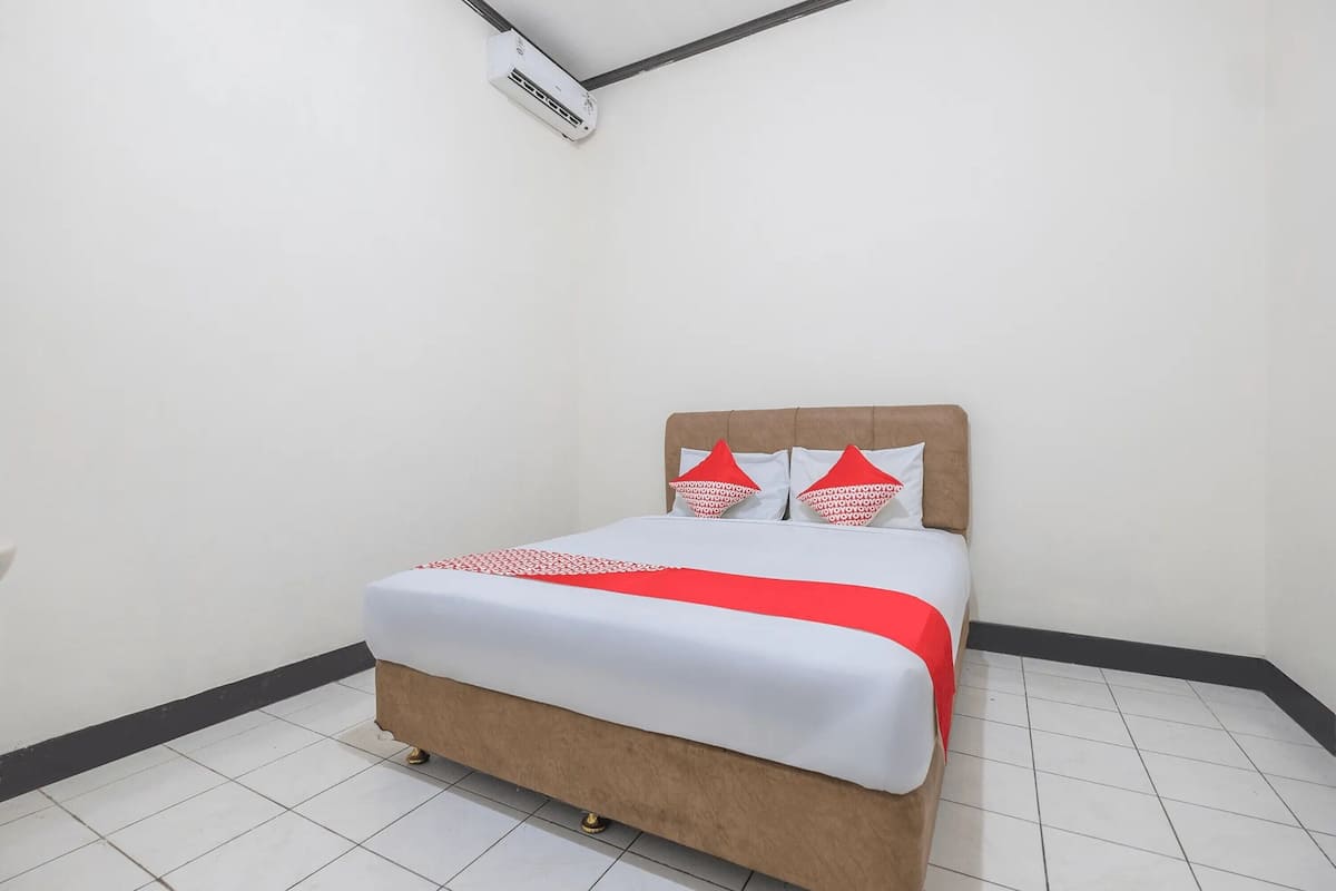 A neatly made bed with a white and red bedspread, a wooden headboard, and two decorative pillows.