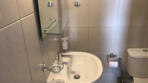 A bathroom with a white sink, glass shelf, and toilet. -  Aphrodites Apartments (Syros)