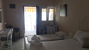 A hotel room with a bed, a desk with a chair, a small table with a chair, and a window with curtains. -  Aphrodites Apartments (Syros)