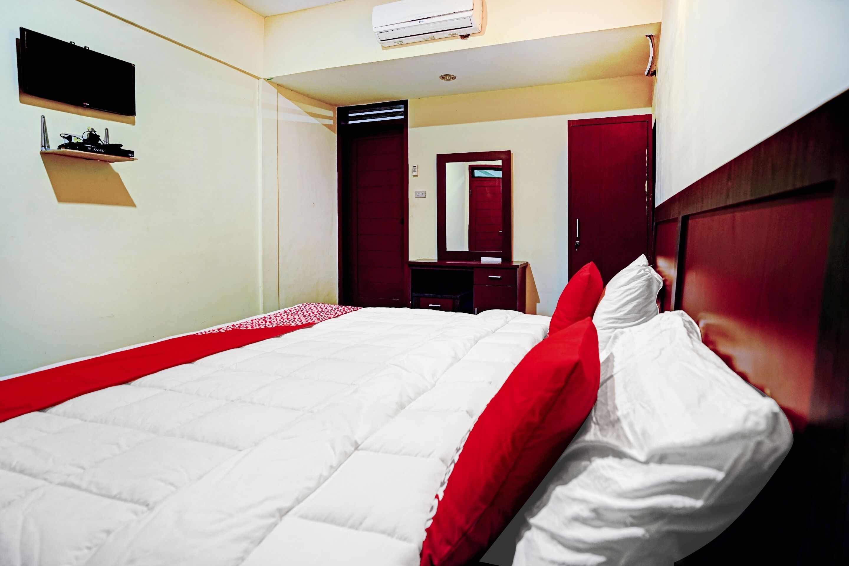 A hotel room with a bed, a TV mounted on the wall, a mirror, and a wardrobe.