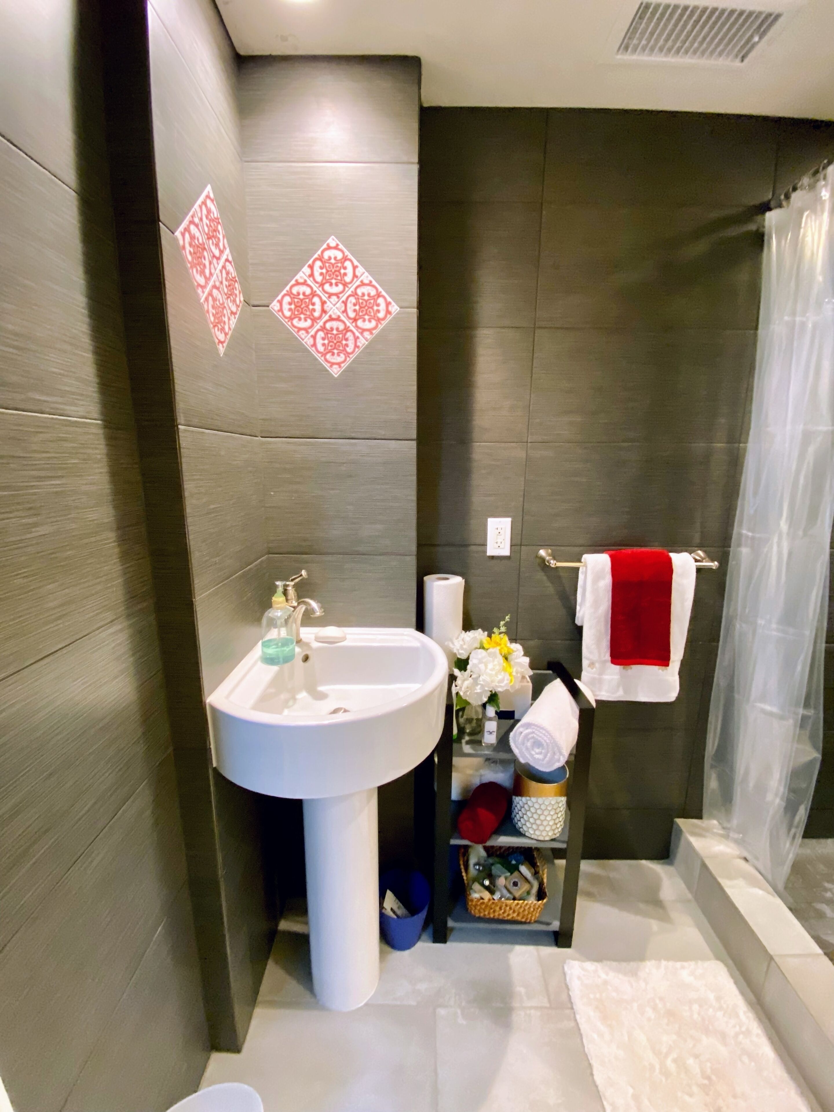 A modern bathroom with a white sink, a glass shower enclosure, and a towel rack with a red towel.