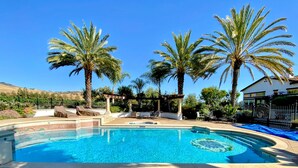 Ein Swimmingpool mit Liegestühlen und Palmen, umgeben von einer Einfriedung und einem Haus.