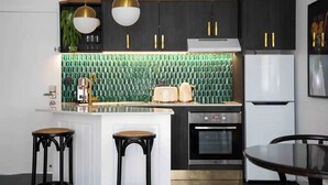Une cuisine moderne avec des meubles noirs, un îlot central blanc et un dosseret de carrelage vert.