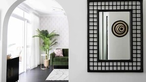 Un salon moderne avec une grande fenêtre, un canapé vert, une plante en pot et une œuvre d’art encadrée de noir accrochée au mur.