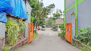 Une ruelle étroite, avec une structure recouverte d’une bâche bleue sur le côté gauche, une porte orange et un petit bâtiment au loin.