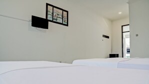 Une chambre d’hôtel avec deux lits, un téléviseur à écran plat fixé au mur et un tableau encadré au-dessus du téléviseur.