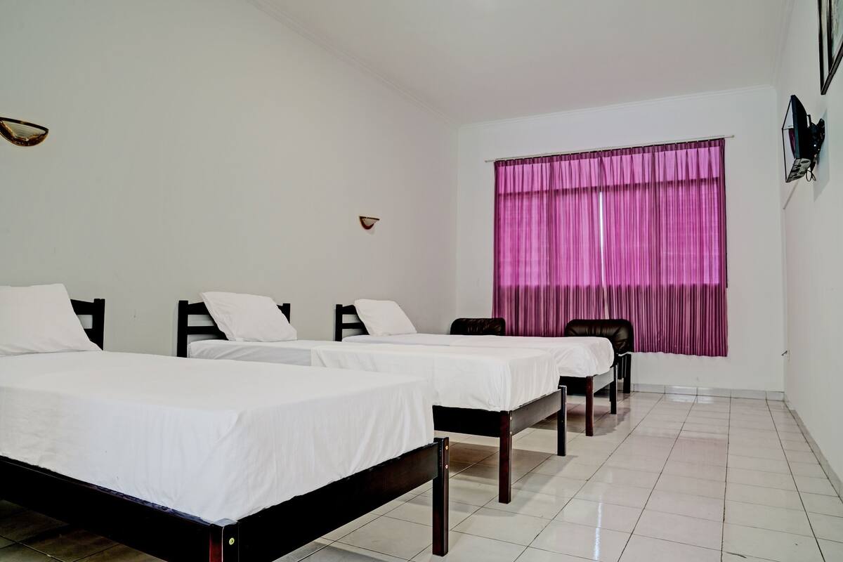 Een hotelkamer met drie eenpersoonsbedden, een raam met roze gordijnen en een betegelde vloer.