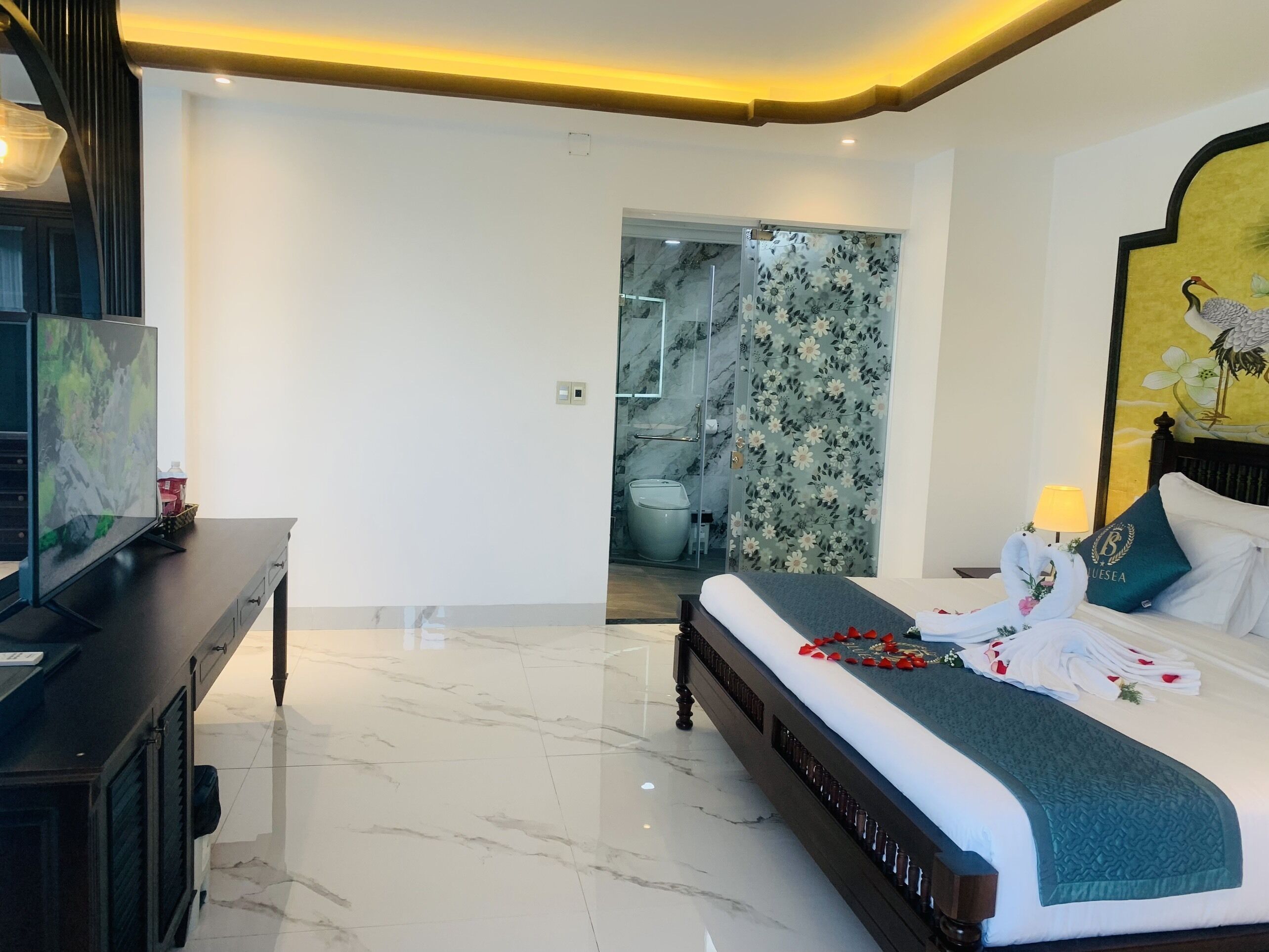 Une chambre d’hôtel moderne avec un grand lit, un bureau et une salle de bain visible à travers une porte en verre.