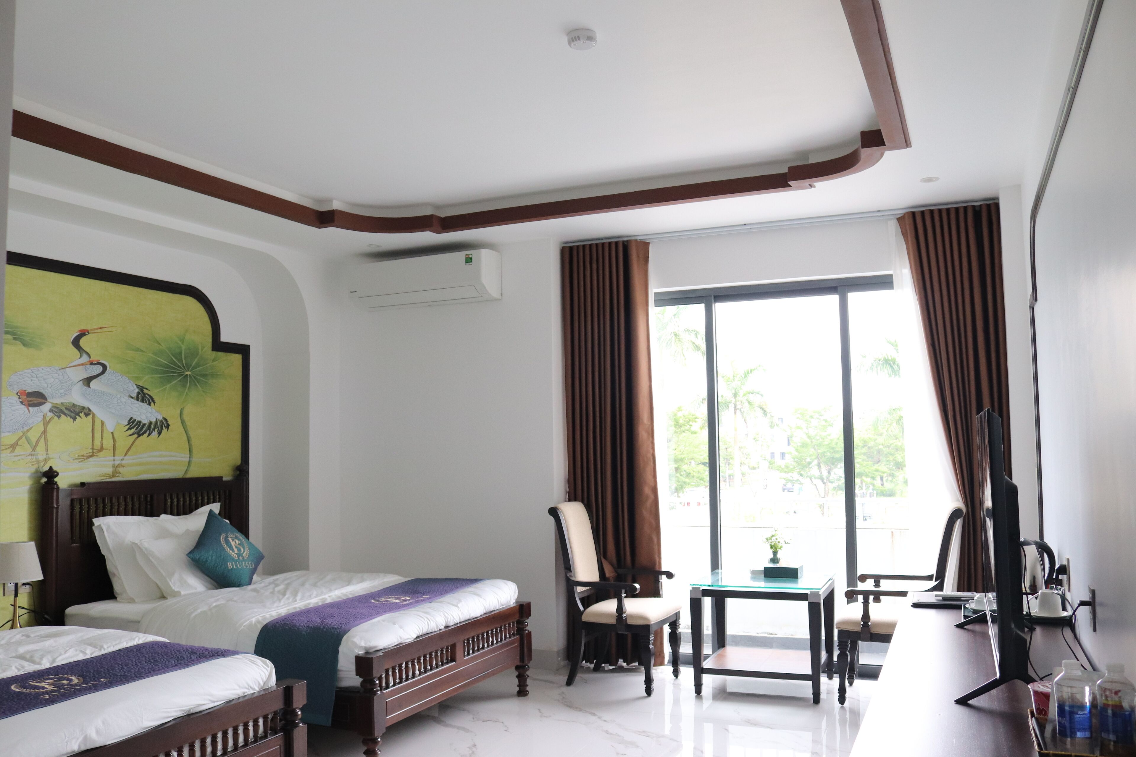 A hotel room with two beds, a desk, a chair, a TV, and a window with curtains.