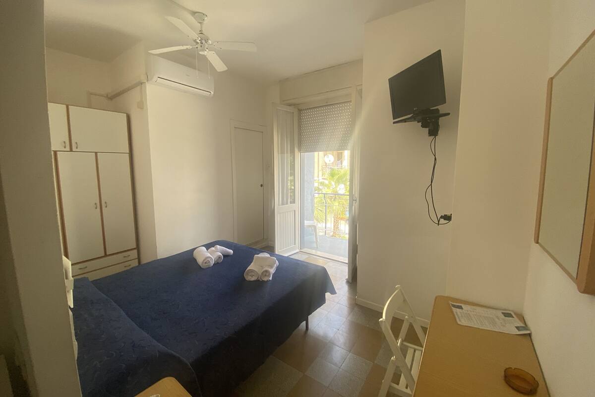 A hotel room with a bed, a desk, a chair, a TV, and a wardrobe.