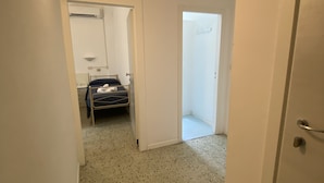 A narrow hallway with a bed in the background, a door with a number, and speckled flooring. - B&B HOTEL LUCCIOLA (Cattolica)