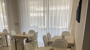 A dining area with tables and chairs, large windows with sheer curtains, and a tiled floor. - B&B HOTEL LUCCIOLA (Cattolica)