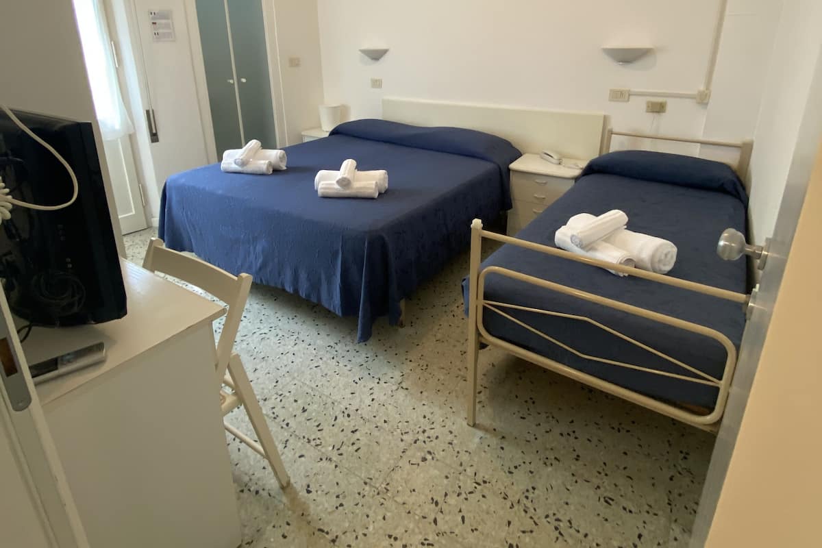 A hotel room with two beds, a desk, a chair, a ceiling fan, and an air conditioning unit.