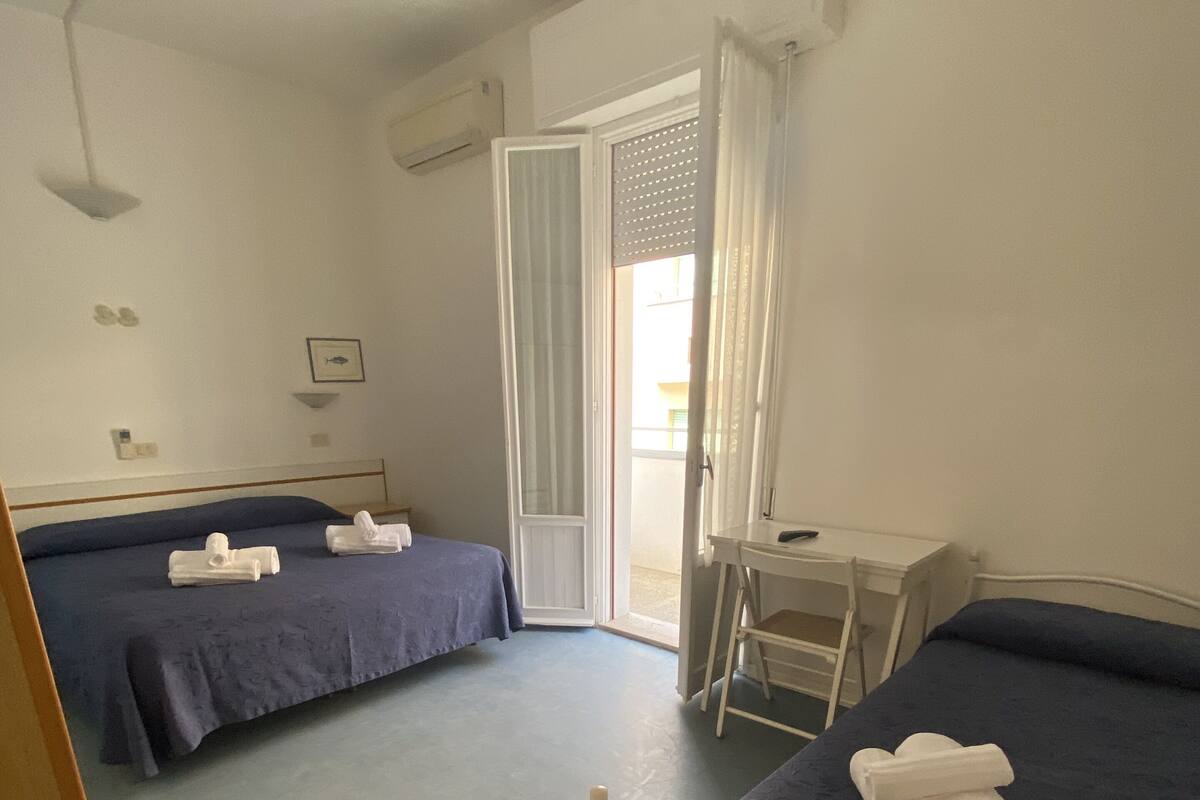 A hotel room with two beds, a desk, and a ceiling fan.