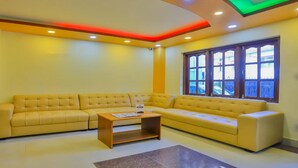 A living room with a yellow sofa, a wooden coffee table, and a window with multiple panes. - MeroStay 113 Hotel TMT (Kathmandu)