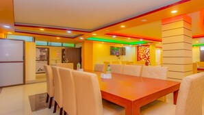 A modern dining area with a wooden table and beige chairs, a water dispenser, and a decorative wall panel. - MeroStay 113 Hotel TMT (Kathmandu)