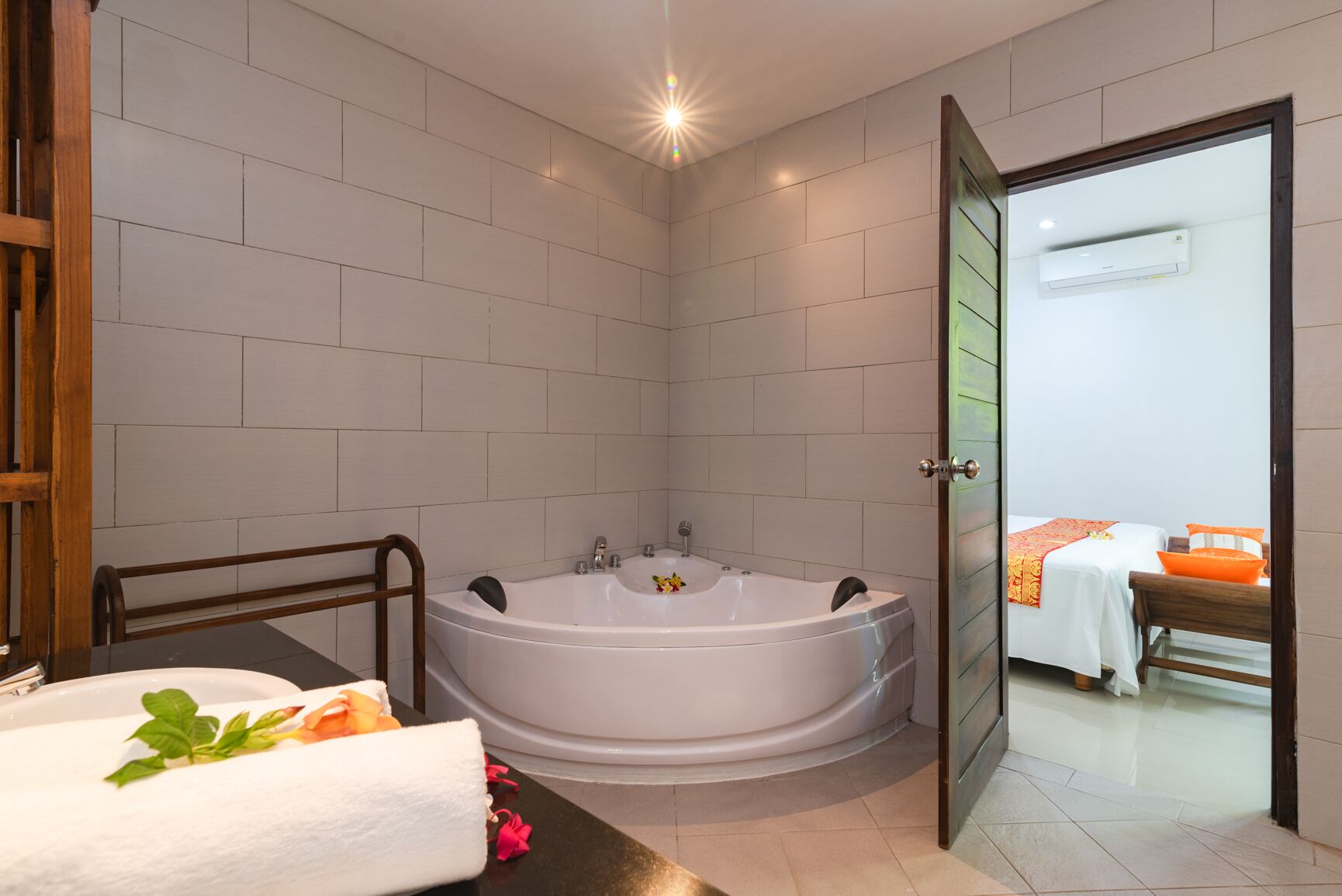 A bathroom with a bathtub, a sink, and a shower area. There is a bed visible through an open door.