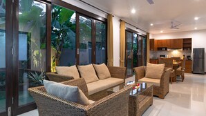 Sala moderna com móveis de vime, uma mesa de centro de vidro e grandes portas de correr que dão para um jardim.