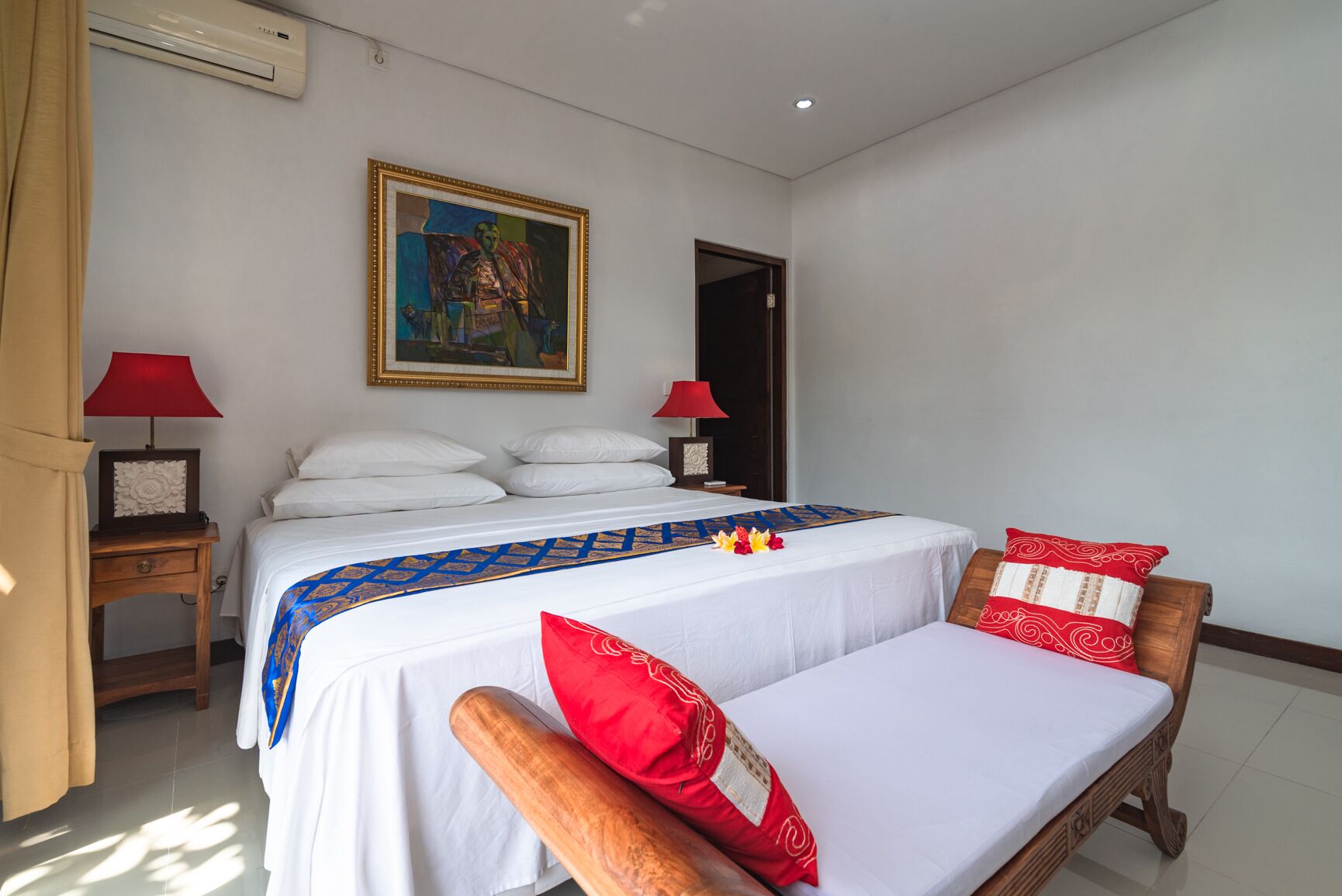 A hotel room with a large bed, two bedside tables with lamps, a painting on the wall, and a wooden chair with red cushions.