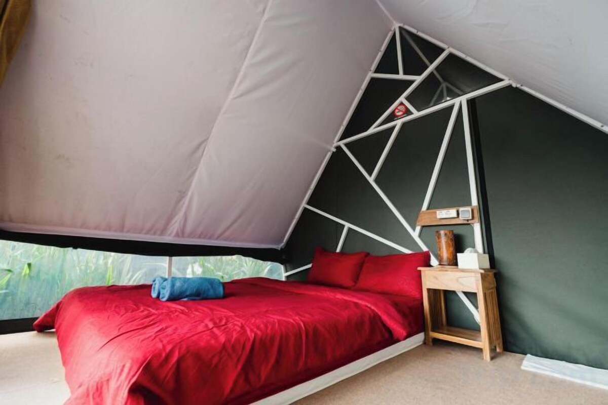 A tent-style bedroom with a bed, pillows, and a bedside table.