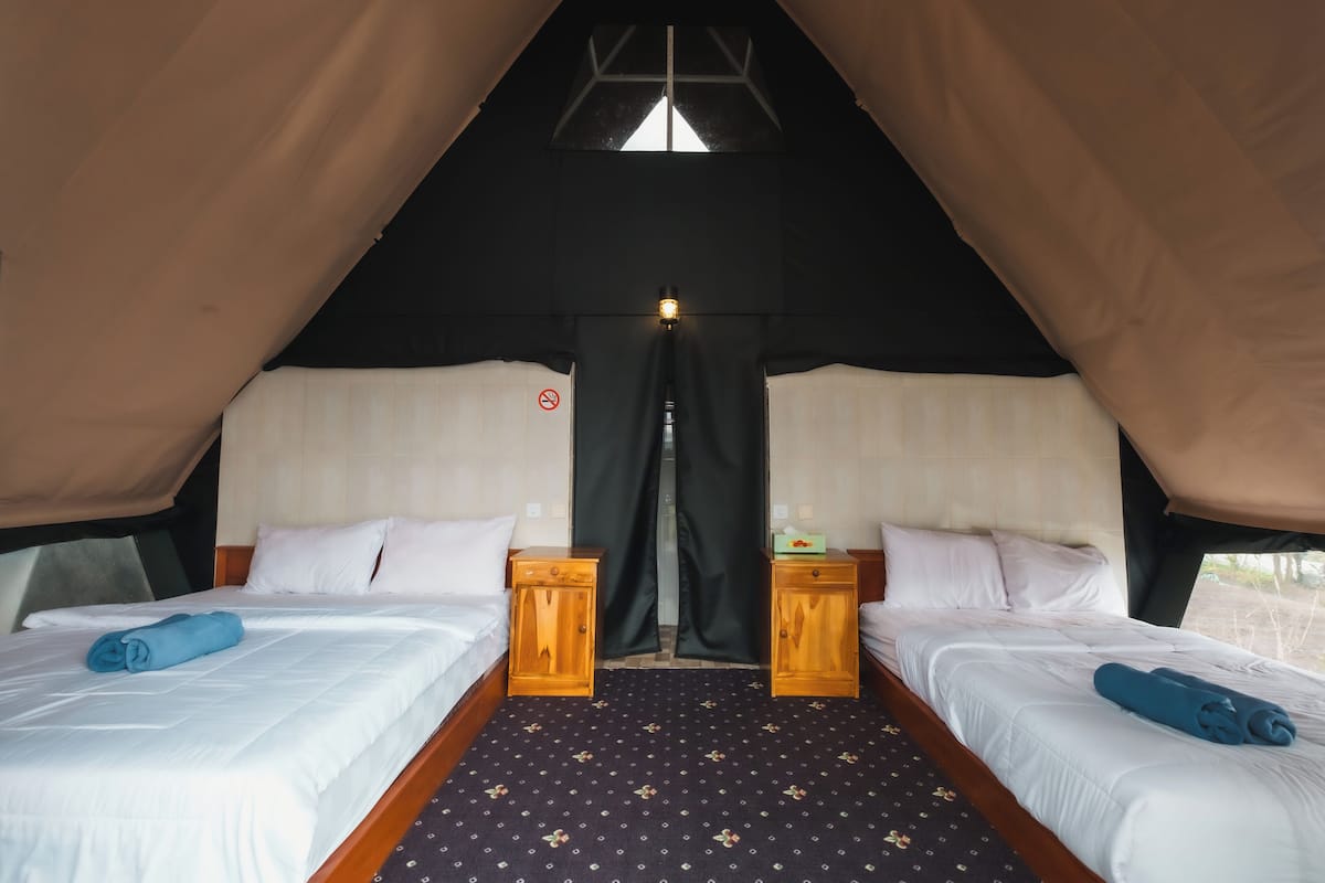 Ein Zelt-ähnliches Zimmer mit zwei Betten, jeweils mit weißer Bettwäsche und blauen Handtüchern, hölzernen Nachttischen und einem gemusterten Teppich.