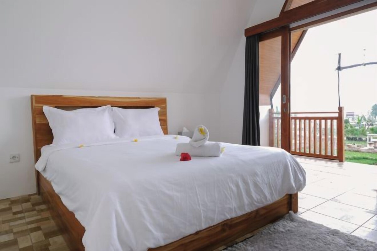 A neatly made bed with white linens and a wooden headboard in a room with a view of the outdoors.
