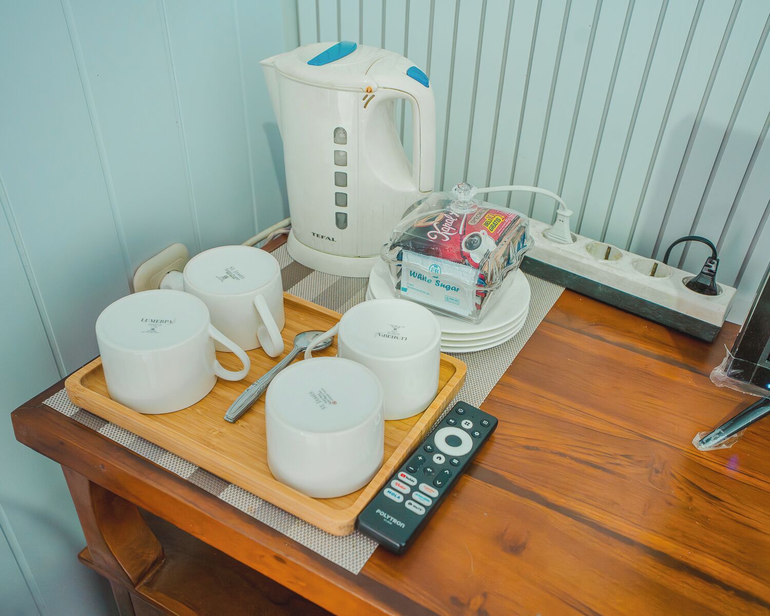 Una kitchenette con una cafetera, un paquete de azúcar blanca y varias tazas blancas sobre una bandeja.