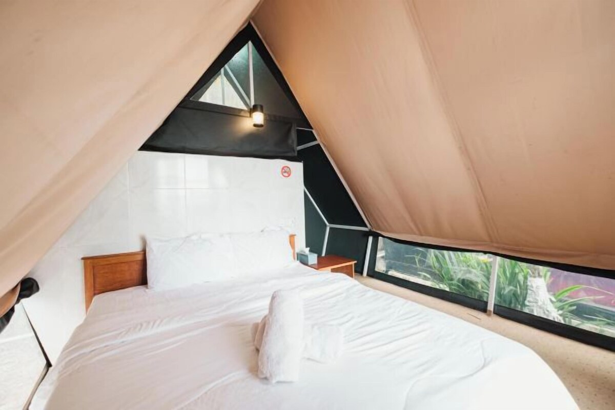 A bedroom with a large bed, a wooden headboard, a nightstand, and a window with a view of greenery.