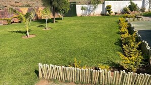 A well-maintained grassy yard with a wooden fence, a gate labeled "BAMERKO," and various shrubs and trees. - Shakwaneng Lodge (Greater Tubatse)