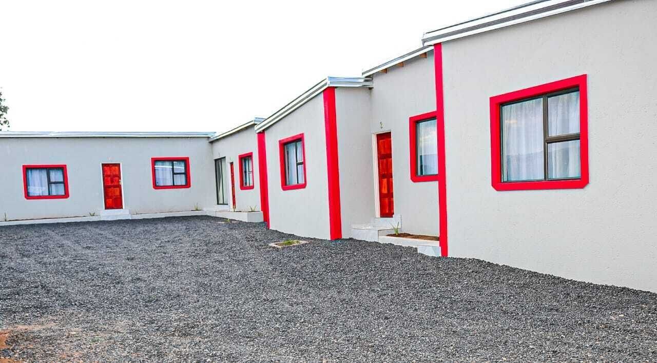 A row of single-story buildings with red-framed windows and doors, a gravel driveway, and a flat roof.