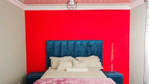 A bedroom with a red wall, a blue headboard, and a pink bedspread. - Shakwaneng Lodge (Greater Tubatse)