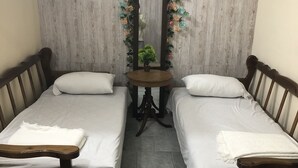 A room with two single beds, a small table, a chair, and a mirror with a floral decoration.